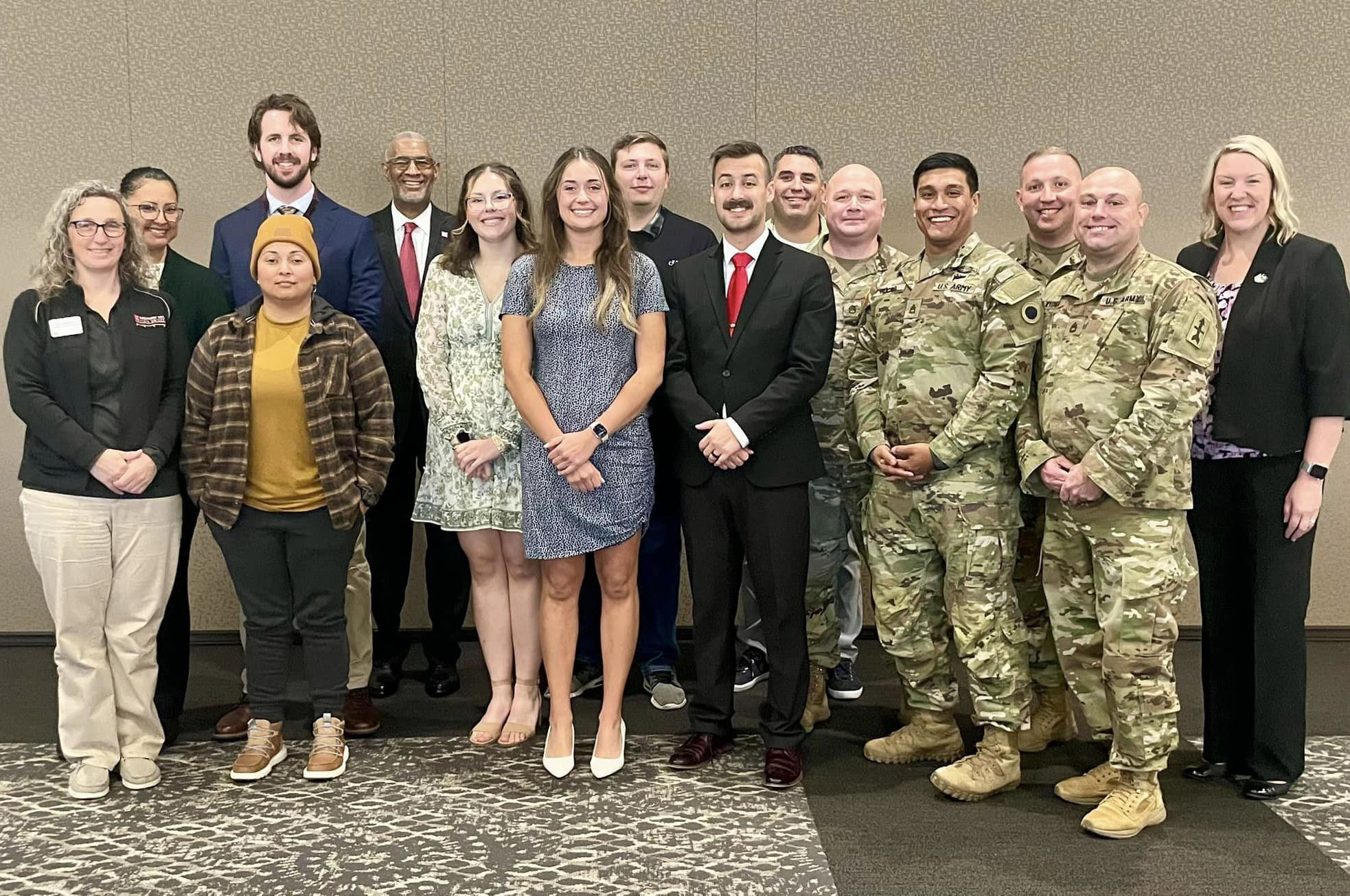 Group of young men and women, some in military fatigues, stand with slightly older gentleman and woman